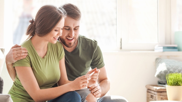A couple smiles as they look together at a pregnancy test, a personal moment alongside discussion of informed male fertility care.